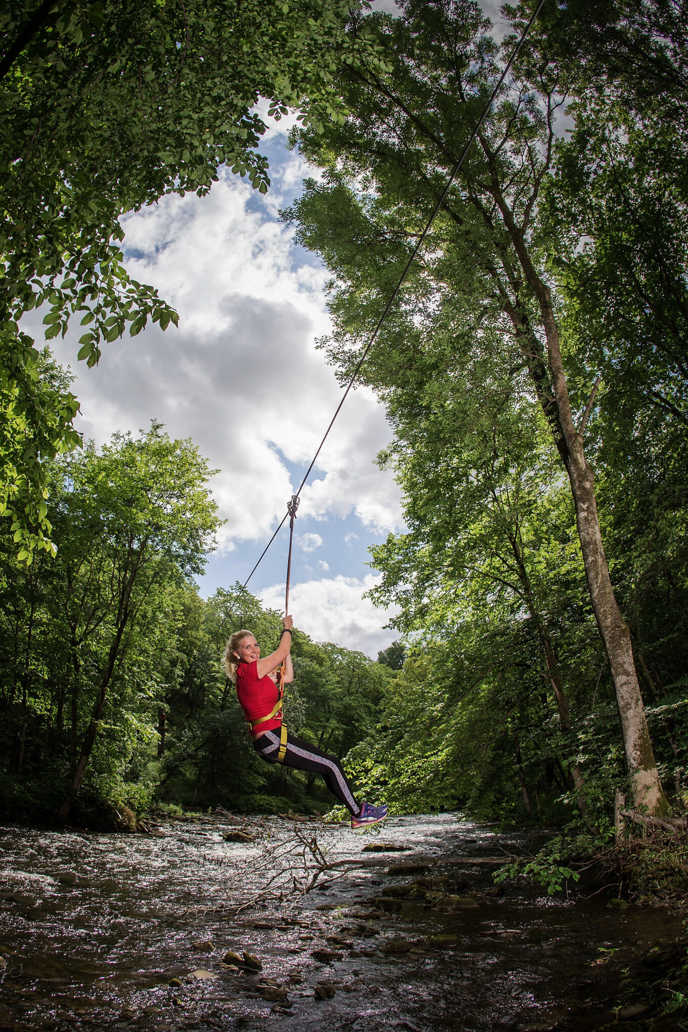 Rõõmus punase pluusiga naine laseb mööda zip-line alla, Kundas Lontova seikluspargis.